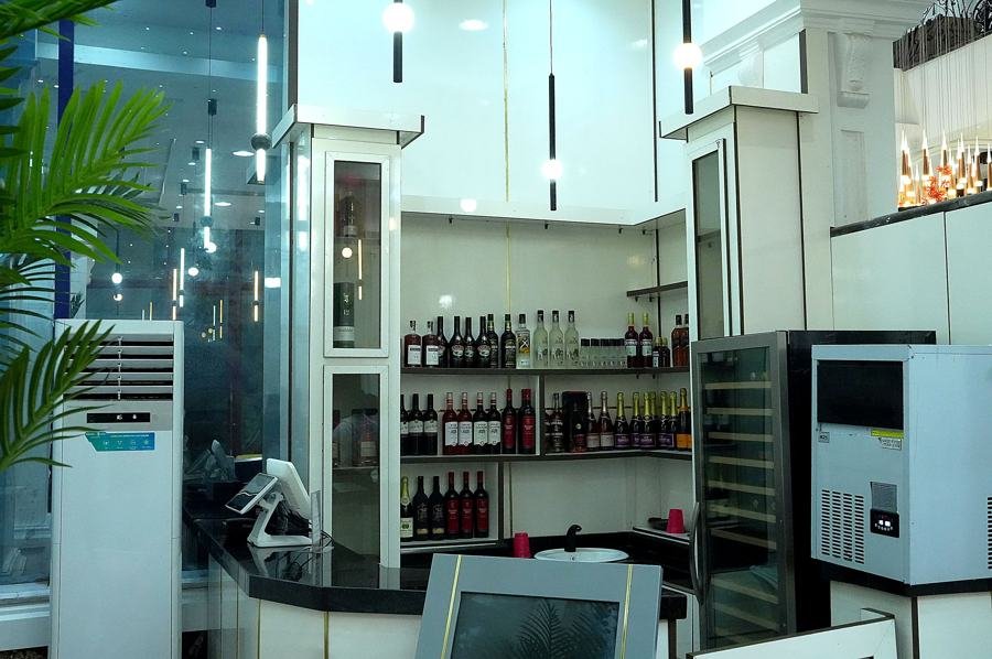 Bar service counter with backlit liquor shelving, wine cooler, ice machine, POS screen and potted palm