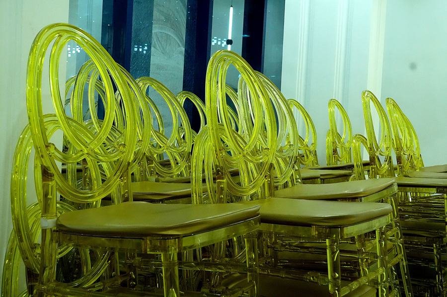 Stacks of translucent gold/yellow chiavari banquet chairs in storage; event-hall furniture rather than a room view