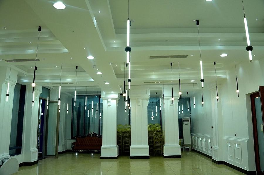Empty white hall lengthwise view with columns and hanging tube lights, open door on left