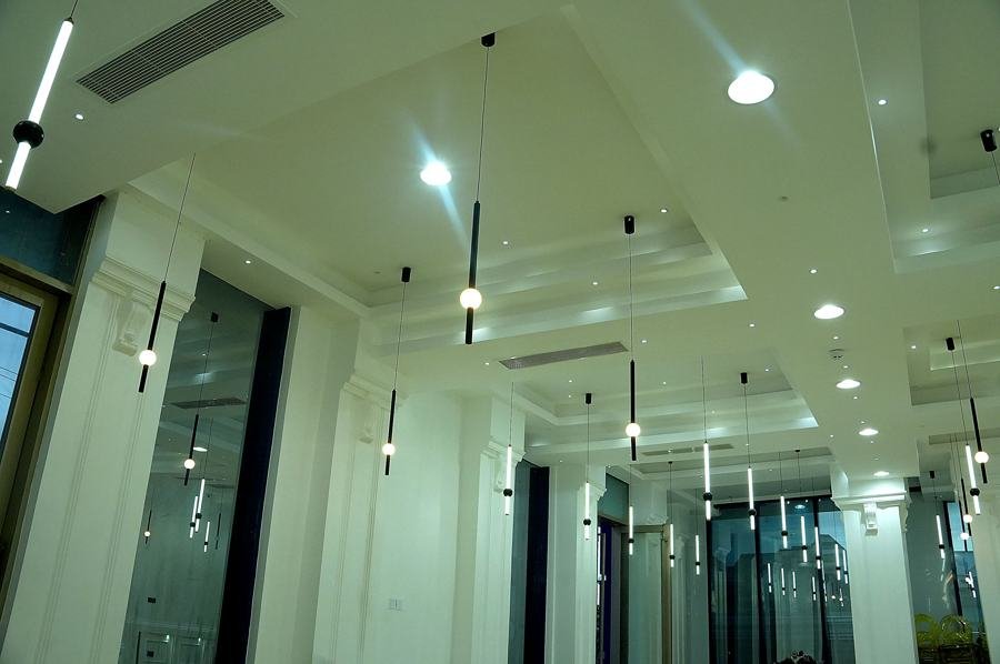 Corner view of the white hall with glass partition doors and pendant tube lights