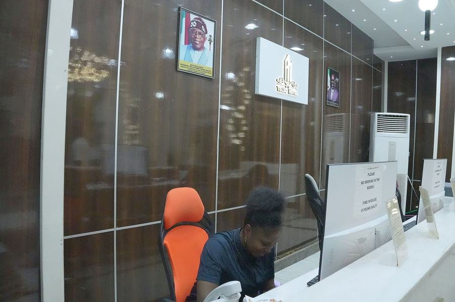 Reception close view with staff member seated in orange chair at counter, dark wood paneling, framed portrait