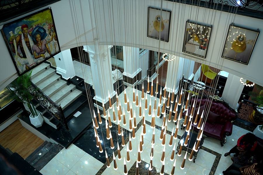 Atrium viewed from above: cascading copper pendant-light installation, staircase, gallery of paintings, purple sofa below