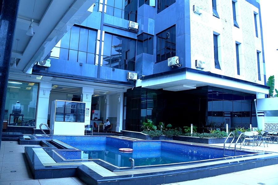 Courtyard swimming pool with orange float ring in foreground, blue glass tower rising behind, loungers at right; strong brand shot