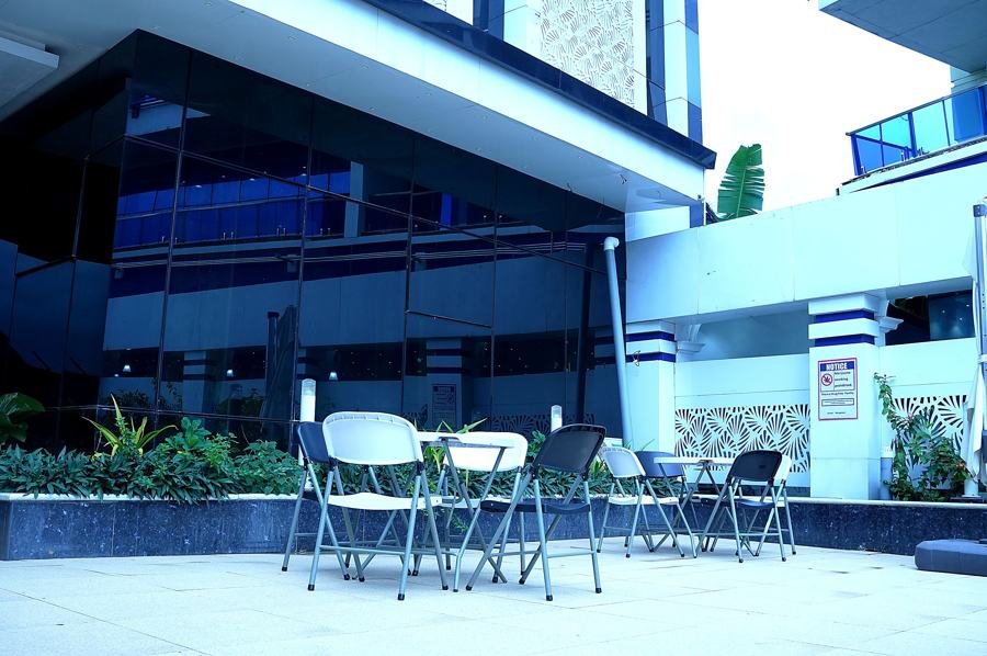 Terrace seating: white folding chairs and tables against dark blue glass curtain wall; unsure between restaurant and other (casual outdoor seating)