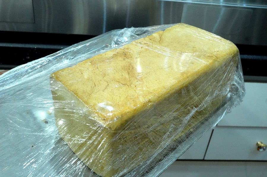 Block of wrapped yam/fufu dough in cling film on kitchen counter; utilitarian prep shot